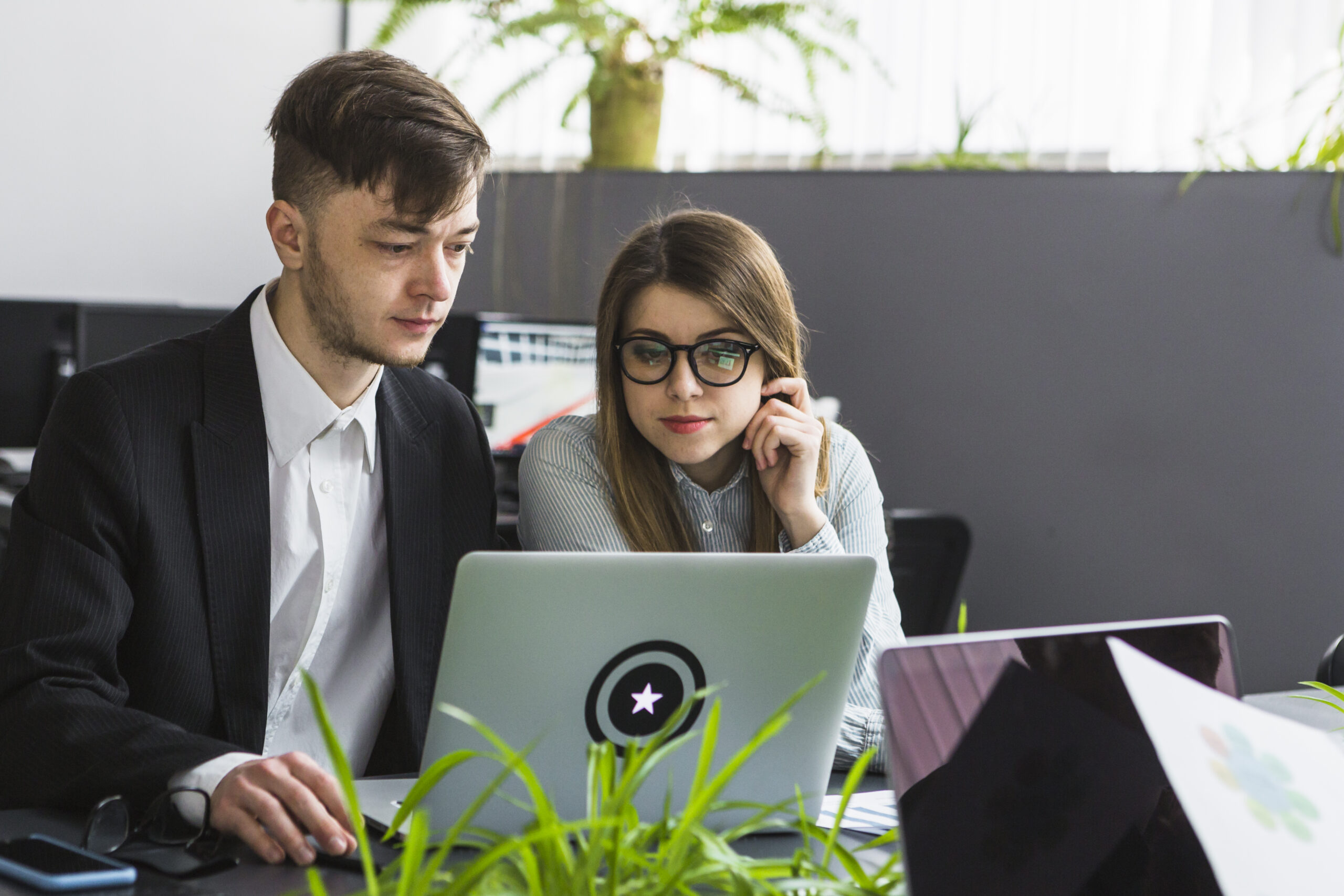 two-young-businesspeople-using-laptop-workplace
